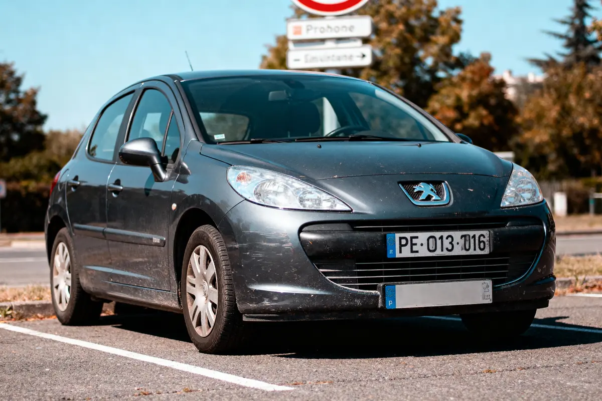 pexels-michal-pech-213601-757318 (1) Voiture Peugeot gris stationnée devant panneau de signalisation, vue de face, par temps ensoleillé.