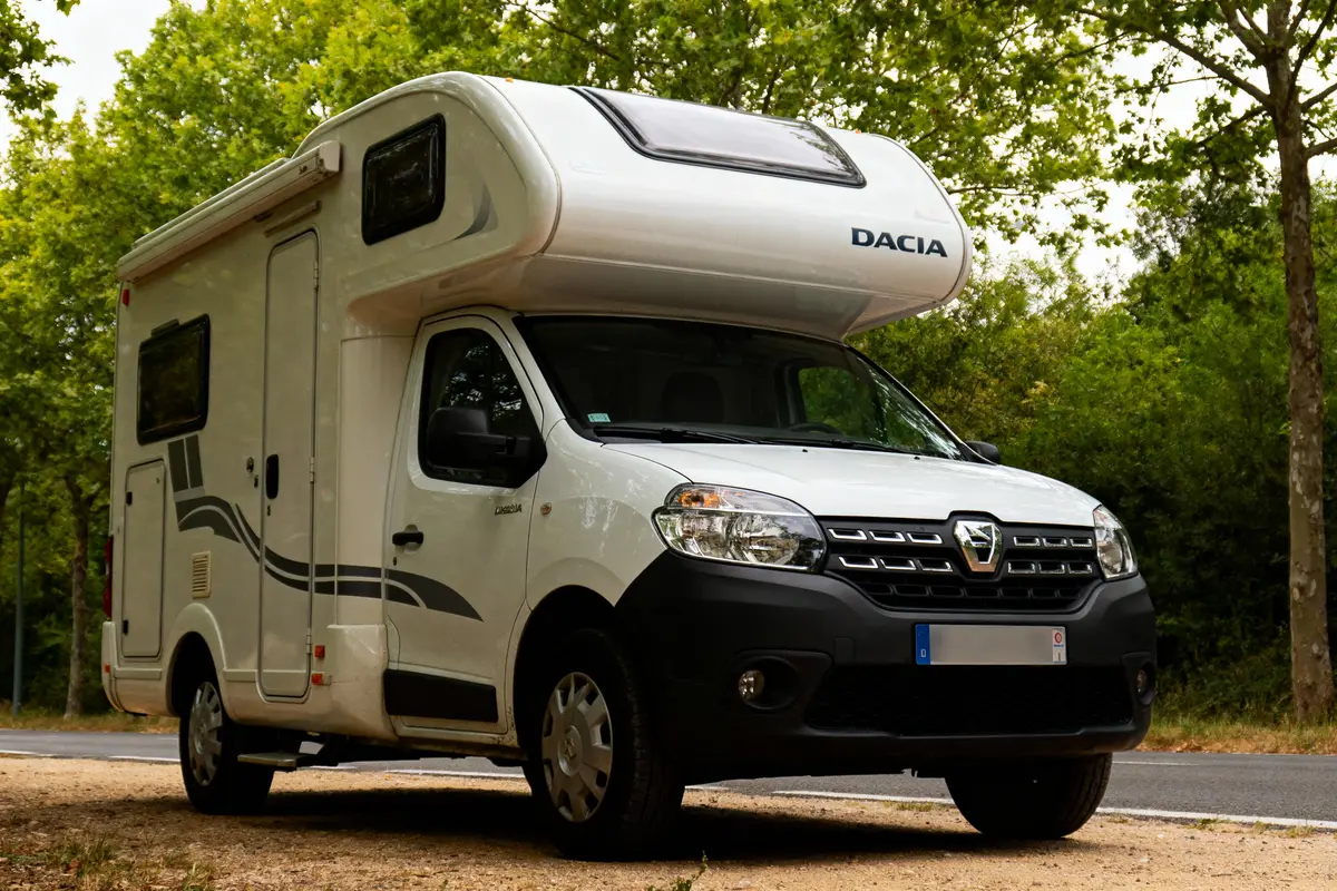 pexels-michal-pech-213601-757318 (1) Camping-car Dacia blanc garé sur le bord de la route, entouré d'arbres verts.