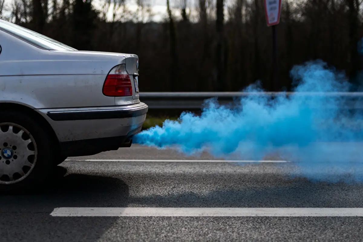 Voiture émettant une fumée bleue par le pot d'échappement sur une route.