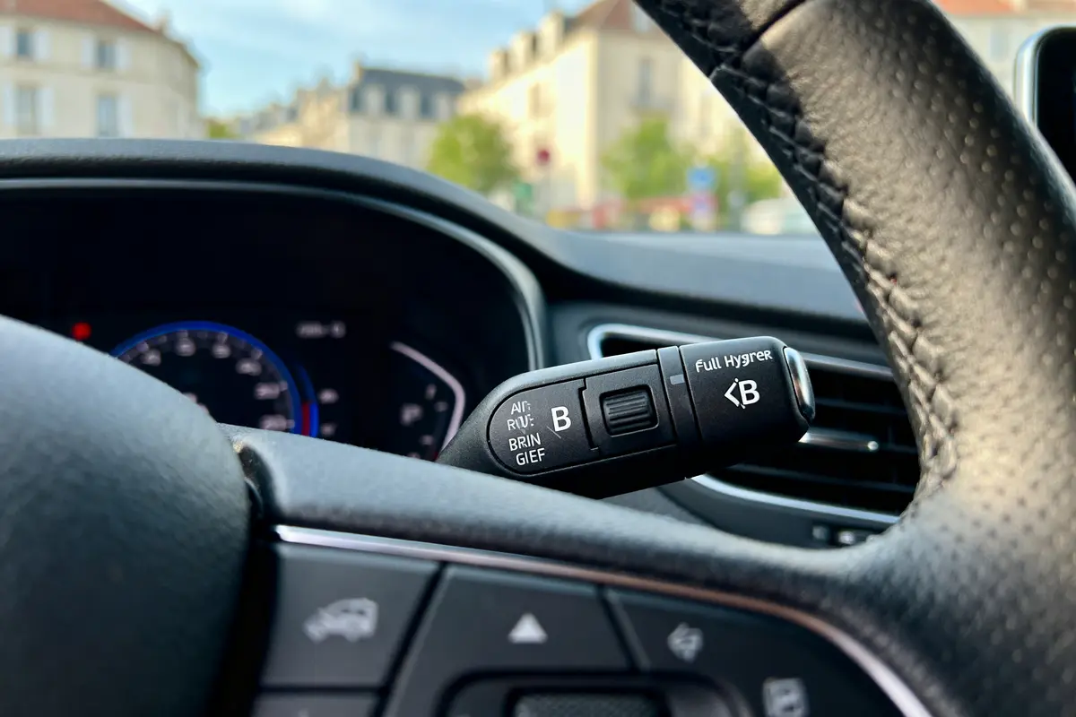 Gros plan sur volant de voiture avec commandes, fond de ville flou.