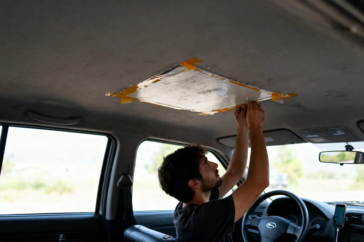 pexels-michal-pech-213601-757318 (1) Homme réparant le plafond d'une voiture avec du ruban adhésif et une planche.