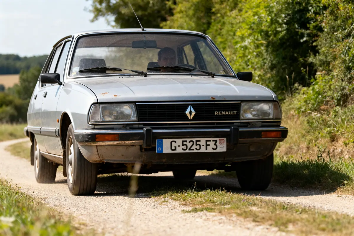 Voiture Renault ancienne sur chemin de terre, entourée de verdure, conduite par une personne. Plaque G-525-F3.