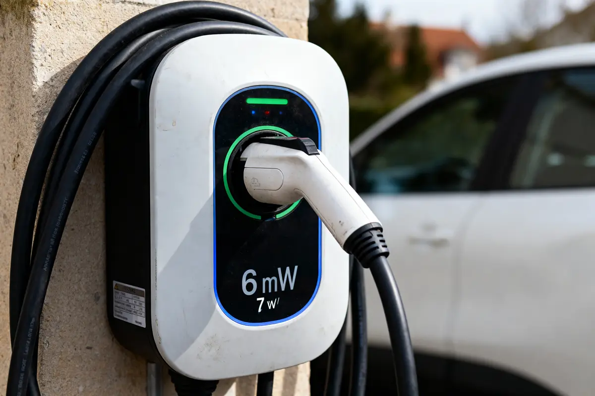 pexels-michal-pech-213601-757318 (1) Borne de recharge électrique avec prise branchée, panneau indiquant "6 mW", voiture blanche en arrière-plan.
