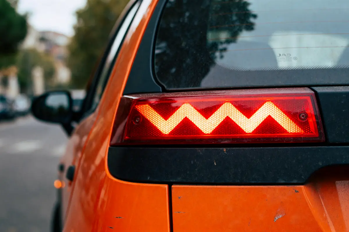 pexels-michal-pech-213601-757318 (1) Feu arrière rouge en motif zigzag sur voiture orange, route floue en arrière-plan.