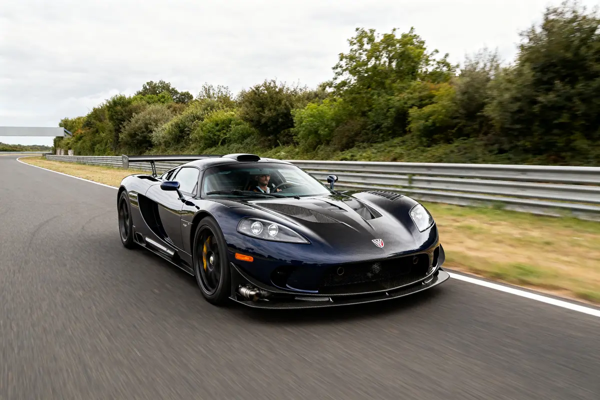 Supercar Hennessey Venom GT noire roulant rapidement sur une piste entourée de végétation luxuriante