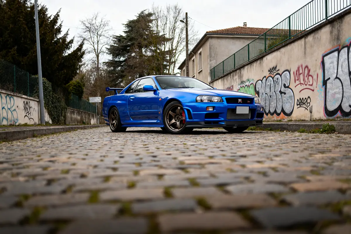 pexels-michal-pech-213601-757318 (1) Voiture R34 Skyline Sedan bleue stationnée dans une rue pavée avec graffitis muraux
