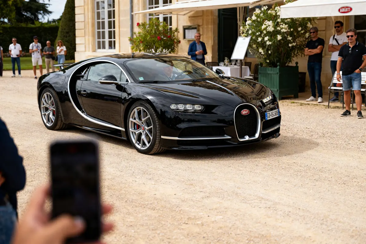 Passants admirant la voiture noire Bugatti stationnée devant un bâtiment élégant