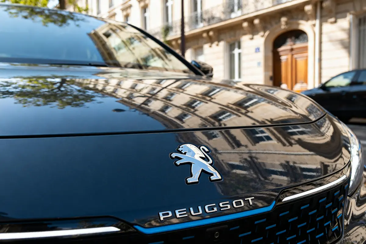 pexels-michal-pech-213601-757318 (1) Voiture arborant le nouveau logo Peugeot avec reflets architecturaux sur le capot noir lustré